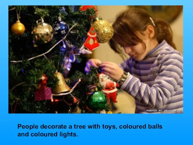 People decorate a tree with toys, coloured balls and coloured lights.