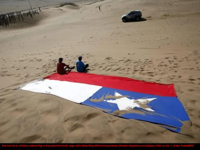 Two men sit on a Chilean national flag as they watch the