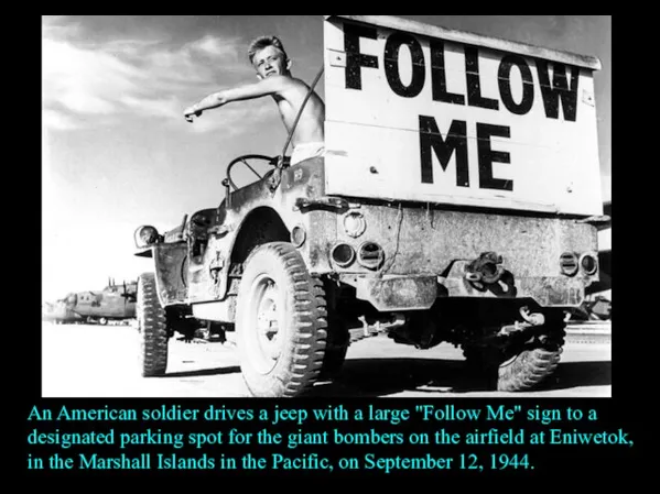 An American soldier drives a jeep with a large "Follow Me" sign