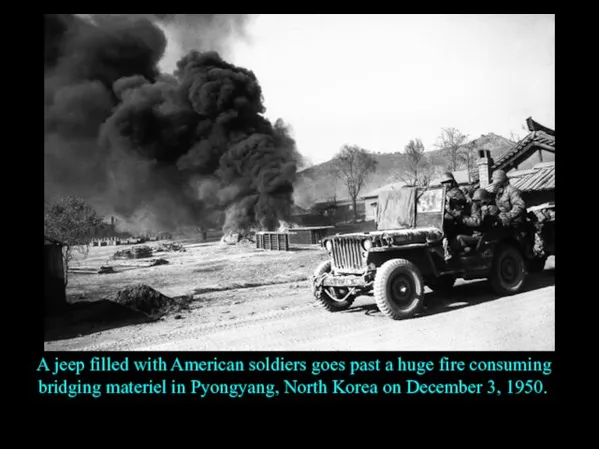 A jeep filled with American soldiers goes past a huge fire consuming